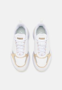 Paire de baskets blanches Puma avec des accents beige, des panneaux en mesh et des lacets blancs, vues de dessus sur un fond clair uni.