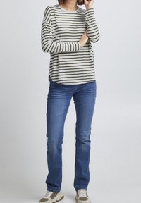 Langärmliges, Rundhals-Shirt mit grünen und weißen horizontalen Streifen; kombiniert mit blauen Jeans und beigen Sportschuhen.