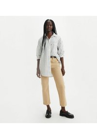 Camisa blanca de manga larga con rayas negras, combinada con pantalones rectos beiges y mocasines negros. Tela ligera, diseño casual.