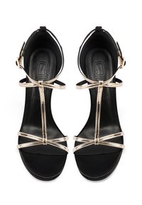 Sandali neri con tacco alto e cinturini metallici dorati, design a T, punta aperta e texture liscia. Caratterizzati da una fibbia regolabile alla caviglia.