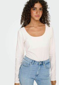 Langærmet hvid top med en rund halsudskæring, parret med lyseblå højtaljede jeans. Glat tekstur, tætsiddende design, minimal detaljer.