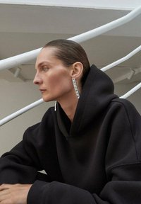 Felpa nera con cappuccio e maniche oversize, abbinata a orecchini brillanti e rettangolari verticali. Tessuto morbido, design minimale.