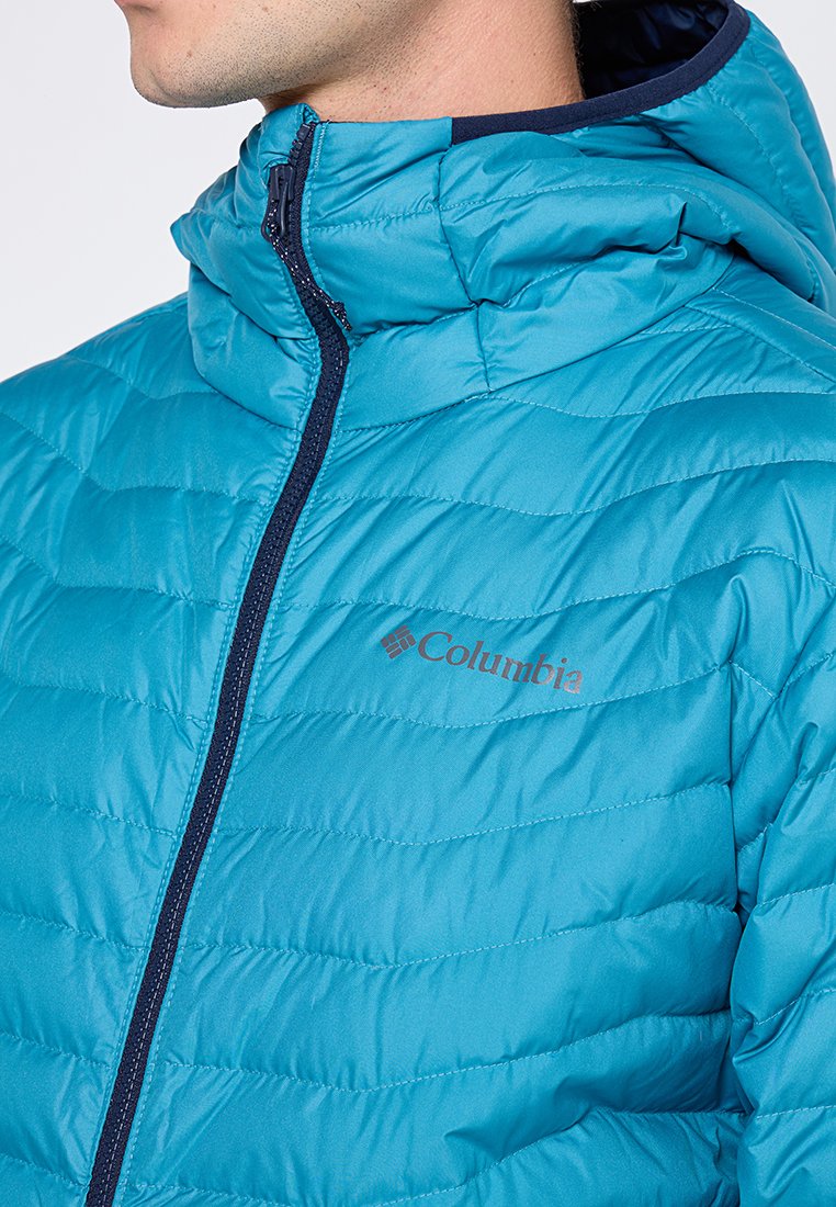 Kurtka puchowa w kolorze akwamarynowym z zamkiem błyskawicznym z przodu, granatowymi akcentami i subtelną pikowaną teksturą. Widoczne logo Columbia na klatce piersiowej.