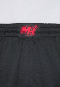 Fekete sportnadrág légáteresztő hálós textúrával. A derékpánton egy piros "MH" logó címke található.