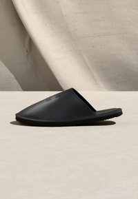 Μαύρο λάστιχο σανδάλι χωρίς λουράκια με υφή στην σόλα, φωτογραφημένο στο πλάι πάνω σε ουδέτερη επιφάνεια και φόντο.