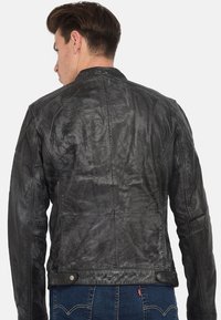 Chaqueta de cuero negro con acabado texturizado, corte entallado y acentos cosidos, que cuenta con un cuello alto y cierres de botones a presión.