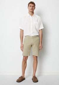Lightweight white linen shirt with short sleeves and a chest pocket, paired with beige cotton shorts and brown slip-on shoes.