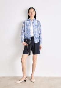 Floral print button-up shirt in blue over a white top, paired with navy shorts and blush slingback heels. Black bag with chain strap.