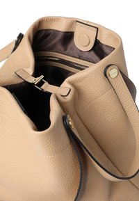 Beige Ledertasche mit strukturierter Oberfläche, ausgestattet mit einem braunen Akzentriemen und goldfarbenen Beschlägen. Offene Oberseite mit einem Reißverschluss-Innenfach.