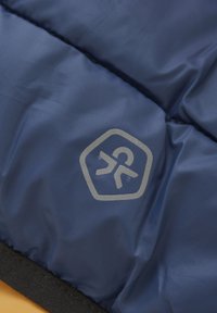 Granatowy, pikowany materiał o teksturowanej powierzchni, z srebrnym logo w heksagonalnym obrysie oraz czarną taśmą na dole.