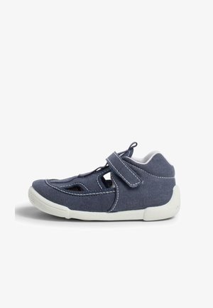 Blauer Stoffschuh mit geschlossenem Zeh und offenen Seiten, ausgestattet mit einem Klettverschluss und weißer Gummisohle. Detaillierte Nähte entlang der Nähte.