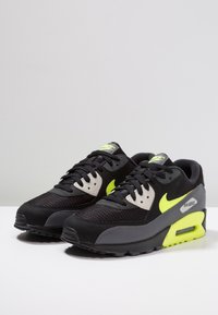 Černá teniska z materiálů síťoviny a kůže, s neónově žlutými akcenty, polstrovaným límcem a viditelnou vzduchovou jednotkou v podrážce.