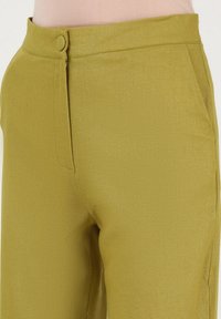 Khakifarbene hoch taillierte Hosen mit glatter Textur, seitlicher Tasche und Knopfverschluss vorne. Taillierter Schnitt und sauberer Saum.