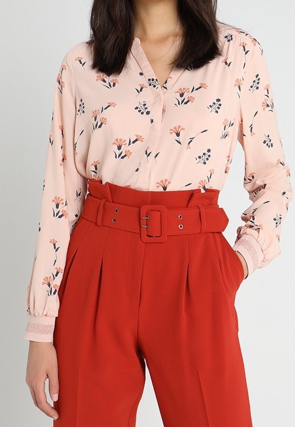 Blusa rosa chiaro con motivo floreale, maniche lunghe e colletto con bottoni abbinata a pantaloni rossi a vita alta con una cintura larga.