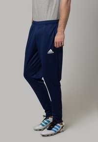 Námořnické sportovní kalhoty z lehké látky, s elastickým pasem, postranními kapsami a malým bílým logem Adidas na levém stehně.