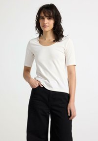 Kremfarvet kortærmet t-shirt med rund hals, tætsiddende pasform og blød tekstur, parret med sorte brede bukser.