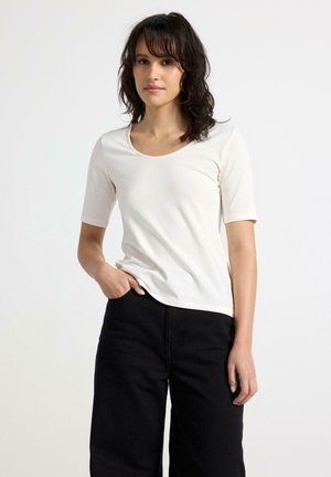 Kremfarvet kortærmet t-shirt med rund hals, tætsiddende pasform og blød tekstur, parret med sorte brede bukser.