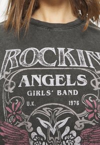 Close-up of gray shirt with worn "ROCKIN' ANGELS GIRLS' BAND U.K. 1976" text and floral winged skull graphic.