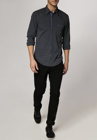 Zwart-wit gestreept overhemd met knopen en lange mouwen, voorzien van een borstzak en een contrasterende kraag. Gecombineerd met een zwarte broek en schoenen.