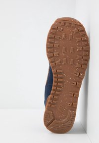 Mörkblå mockaskor med en texturerad brun gummisula, med djupa mönster och prickar, designade för grepp och hållbarhet.