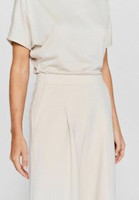 Light beige blouse with short sleeves and relaxed fit, paired with wide-leg trousers featuring a high waist and front pleats.