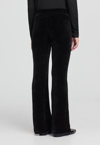 Pantaloni a zampa d'elefante in corduroy nero con superficie testurizzata. Progettati con una vita alta per il massimo comfort e una finitura liscia.