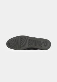 Suela de zapato de goma negra con patrón de agarre texturizado y detalles de logo. Forma redondeada con un borde ligeramente elevado. Acabado mate suave.