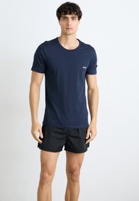 Marineblå t-skjorte med kort erm laget av myk bomull, med rund hals, med en liten hvit "BOSS"-logo på venstre bryst. Svarte shorts.