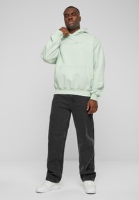 Mintgrønn hettegenser med frontlomme og elastiske mansjetter, kombinert med mørkegrå jeans og hvite sneakers. Enkel, uformell design.