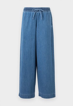 Luźne niebieskie spodnie z denimu z elastycznym pasem i sznurkiem z przodu, prezentowane na białym tle.