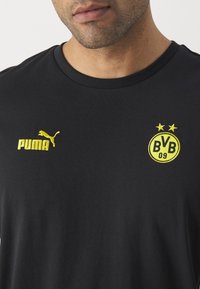 Man i svart Puma-t-shirt med gult Puma-logotyp på vänster sida och Borussia Dortmund BVB 09-emblem på högra bröstet.