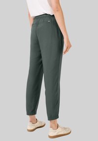 Dark green, lightweight trousers with an elastic waistband, tapered legs, and a single back pocket, paired with beige sneakers.