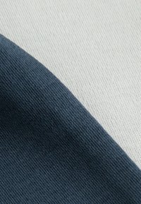 Due tessuti sovrapposti: blu scuro e beige, entrambi con una trama fine, che mostrano una transizione fluida tra i colori.