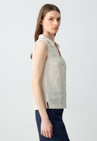 Camicetta senza maniche in lino color beige chiaro con colletto a notched, chiusura frontale a bottoni e spacco laterale. Tessuto morbido, vestibilità casual.
