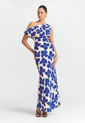 Maxikleid in Creme mit großem blauen Blumendessin. Mit schulterfreier Rüschendetails und taillierter Silhouette. Schwarze Absatzsandalen.