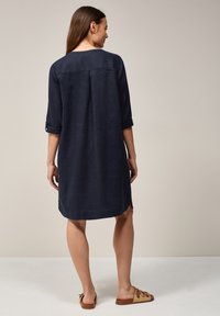 Granatowa lniana sukienka z rękawami o długości trzy czwarte, z detalem w postaci zakładki na plecach, bocznymi rozcięciami i luźnym krojem. Połączona z beżowymi sandałami na płaskiej podeszwie.