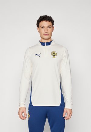 Camiseta deportiva de manga larga en crema con acentos en azul marino, con un alto cuello y el emblema de Portugal. Fabricada en un tejido texturizado y transpirable.
