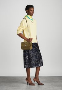 Dzeltena adīta džemperis, tumši zila sequīno svārki, olīvu krāsas quilted rokassoma un brūni augstpapēžu sandales. Modelis valkā zilu un zaļu šalli.