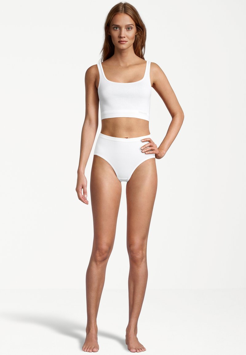 Witte katoenen crop top met brede schouderbanden en high-waisted onderbroek, beide met een gladde textuur en een eenvoudig ontwerp. Model staat blootsvoets.