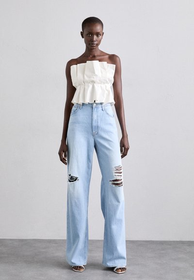 Vit strapless topp med utflugen fåll och veck, i kombination med ljusblå vida jeans med slitningar och revor.