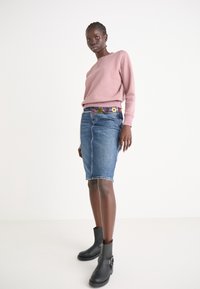 Sweatshirt rose avec un col rond, associé à une jupe en denim bleue et des bottines noires à la cheville. La ceinture décorative présente des motifs floraux.