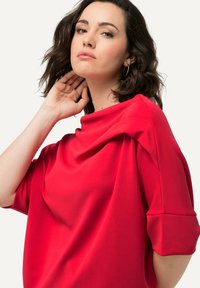 Top rouge drap�é avec une texture douce, des manches courtes et une coupe décontractée. Il présente un col rond et une surface lisse.