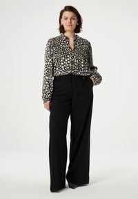 Black and white patterned long-sleeve blouse with a collar, paired with high-waisted black trousers. Flat shoes with studded accents.