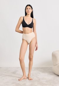 Μαύρο σουτιέν bralette με V λαιμόκοψη, σε συνδυασμό με εσώρουχο σε υψηλή μέση σε nude απόχρωση. Λείο υλικό, απλός σχεδιασμός και ουδέτερη χρωματική παλέτα.