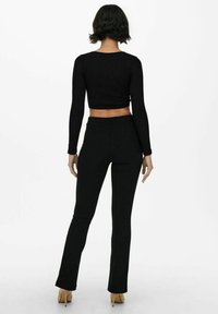 Svart, långärmad cropped topp kombinerad med åtsittande svarta utsvängda byxor. Outfiten har en mjuk textur och en minimalistisk design.