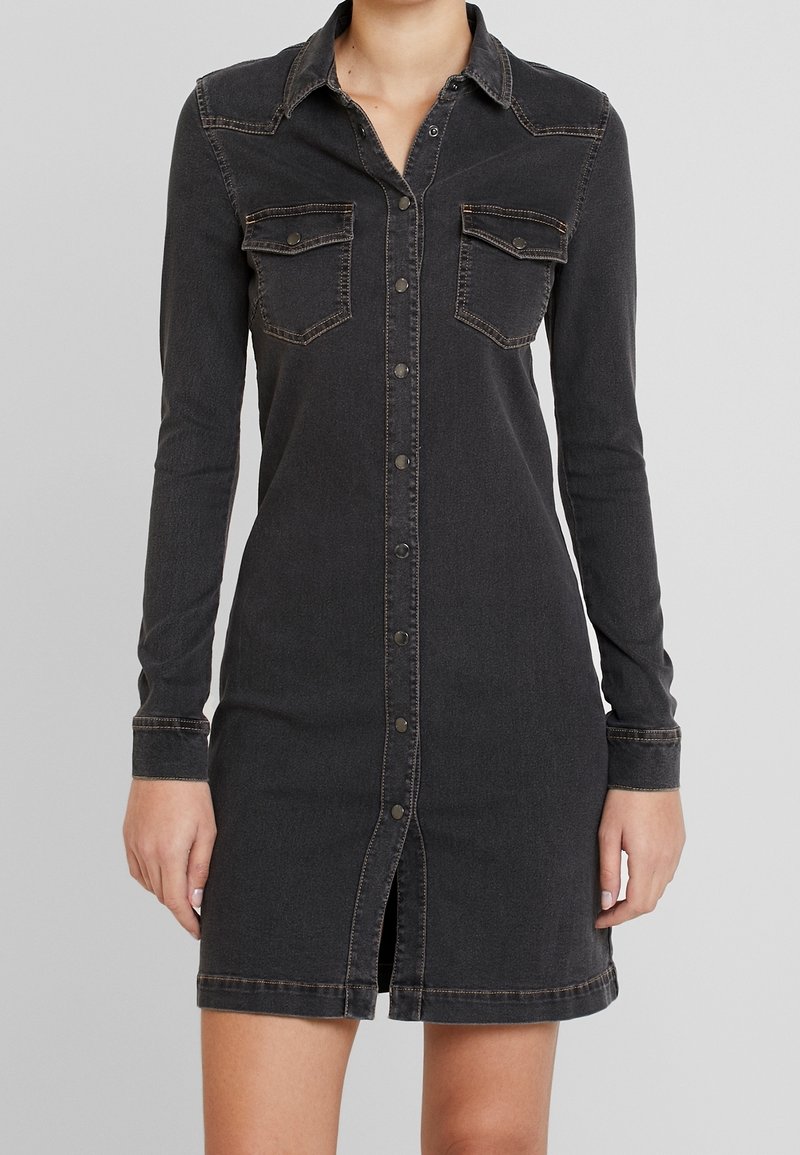 Musta farkkutunikkamekko pitkillä hihoilla, nappisuljenta, rintataskut ja kontrastiväriset ompeleet. Mukana on edessä aukeava malli ja keskivartalon pituus.