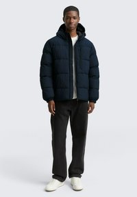 Giubbotto imbottito blu navy con cappuccio, design trapuntato, chiusura a zip e tasche laterali. Abbinato a jeans neri e sneakers bianche.