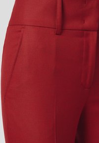 Czerwone spodnie o teksturowanym wzorze i dopasowanym kroju, z bocznymi kieszeniami i gładkim paskiem w talii. Materiał ma subtelny wzór i bogaty odcień.