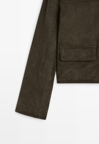 Dark green suede jacket with a textured finish, featuring a straight-cut sleeve and a patch pocket on the front.