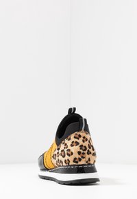 Sneaker med svart lacktå, gul mockafront och baksida med leopardtryck. Har en dragflik och en vit mellansula.